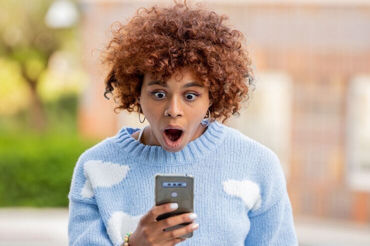 Donna guarda stupita il suo cellulare, a bocca aperta